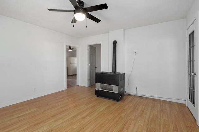 spare room with a ceiling fan, a wood stove, light wood-style floors, and baseboards