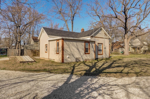 view of side of home with a chimney, roof with shingles, a yard, and fence