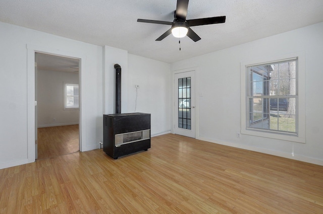 unfurnished living room featuring baseboards, ceiling fan, light wood-style flooring, a wood stove, and a textured ceiling