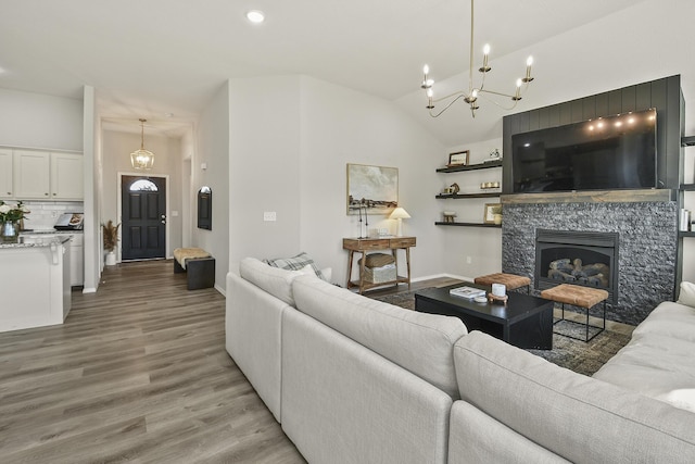 living area with baseboards, a stone fireplace, vaulted ceiling, light wood-type flooring, and a chandelier