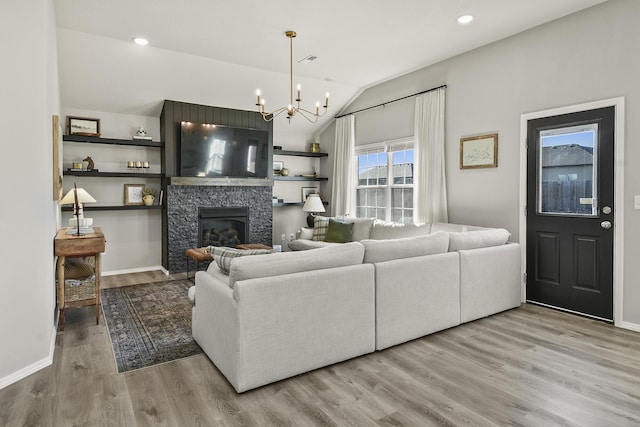 living area with visible vents, vaulted ceiling, a fireplace, an inviting chandelier, and wood finished floors