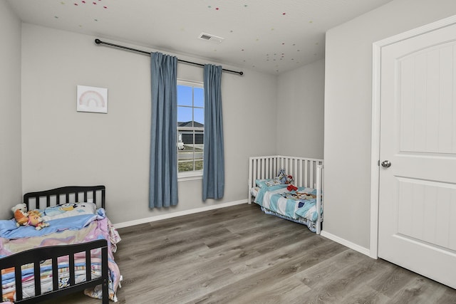 bedroom with wood finished floors, visible vents, and baseboards