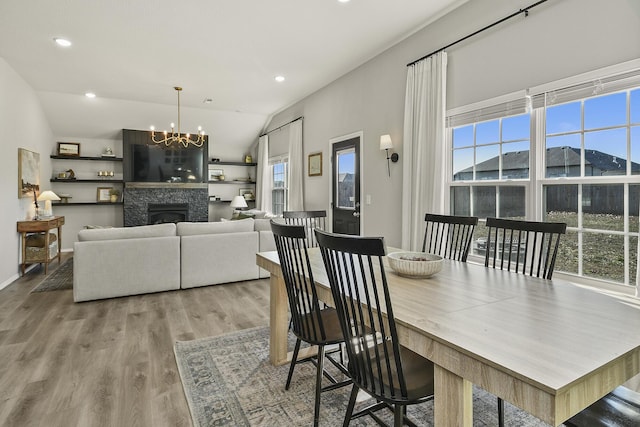 dining area with wood finished floors, recessed lighting, an inviting chandelier, a fireplace, and lofted ceiling