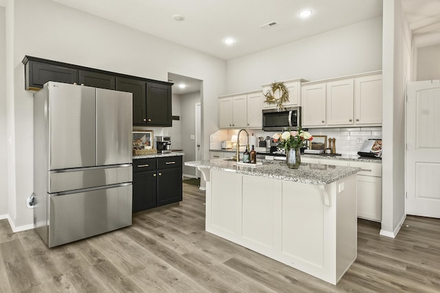 kitchen with visible vents, a kitchen island with sink, backsplash, stainless steel appliances, and light wood-style floors