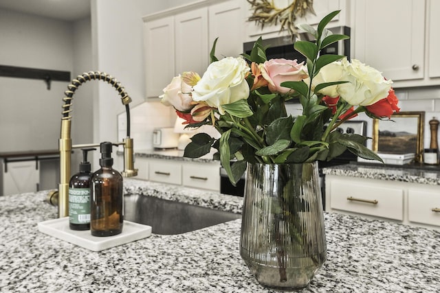 interior details with white cabinets, light stone countertops, and a sink