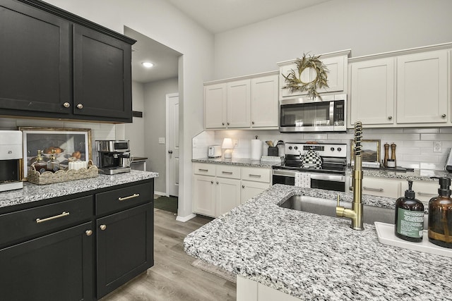 kitchen with stainless steel appliances, white cabinetry, dark cabinets, and light wood-style flooring