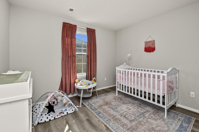 bedroom featuring visible vents, a crib, baseboards, and wood finished floors