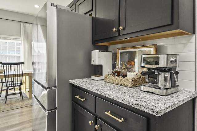 kitchen with light stone countertops, light wood-style floors, dark cabinets, and freestanding refrigerator