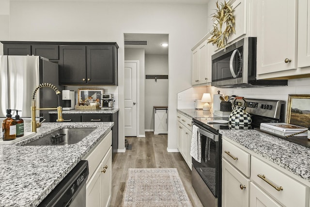 kitchen featuring light wood finished floors, visible vents, backsplash, appliances with stainless steel finishes, and a sink