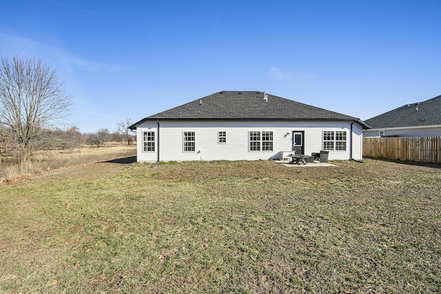 rear view of property featuring fence, roof with shingles, a yard, a fire pit, and a patio area