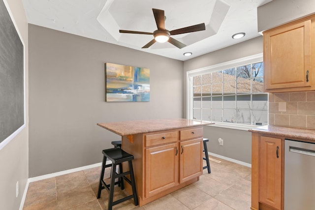 kitchen featuring a breakfast bar area, light brown cabinets, baseboards, dishwasher, and backsplash