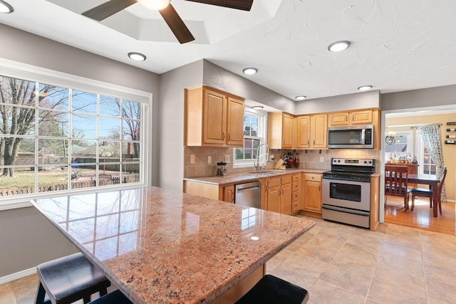 kitchen featuring light stone countertops, light brown cabinetry, decorative backsplash, stainless steel appliances, and a sink