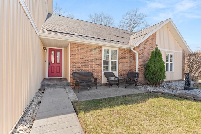 entrance to property with a yard, a patio, brick siding, and roof with shingles