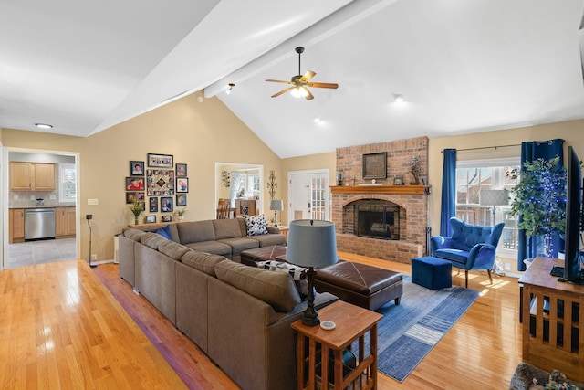 living room featuring a ceiling fan, high vaulted ceiling, beam ceiling, a fireplace, and light wood-style floors