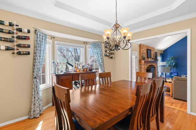 dining room featuring a brick fireplace, light wood-type flooring, baseboards, and crown molding