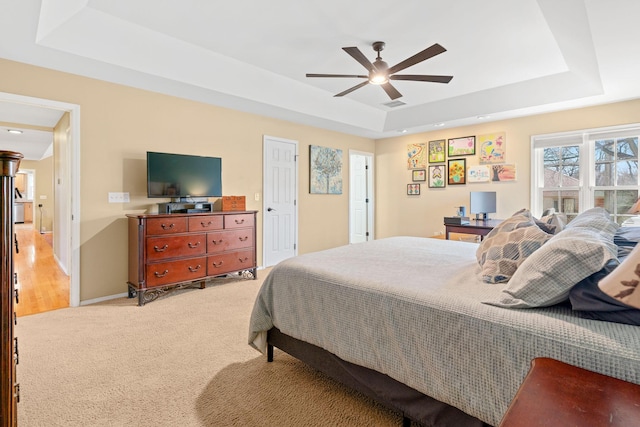 bedroom featuring visible vents, baseboards, a tray ceiling, light carpet, and a ceiling fan