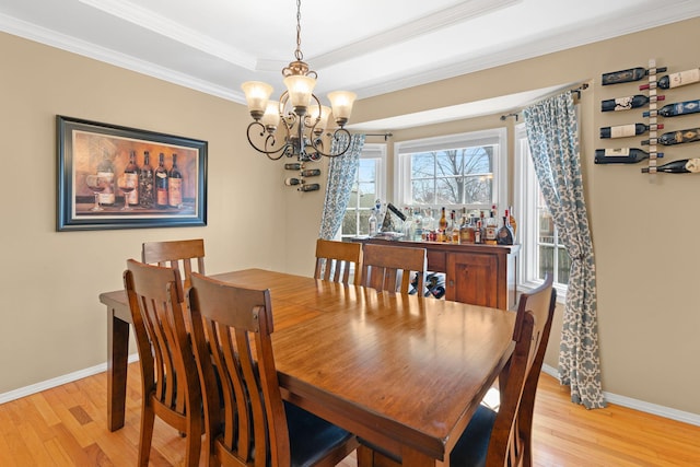 dining area featuring a tray ceiling, baseboards, light wood-type flooring, and ornamental molding