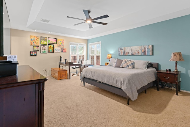 bedroom with visible vents, a ceiling fan, a tray ceiling, baseboards, and light colored carpet