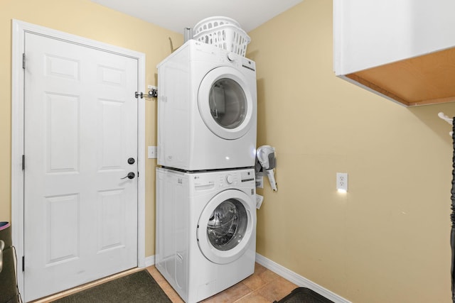 clothes washing area featuring light tile patterned floors, laundry area, baseboards, and stacked washer and dryer