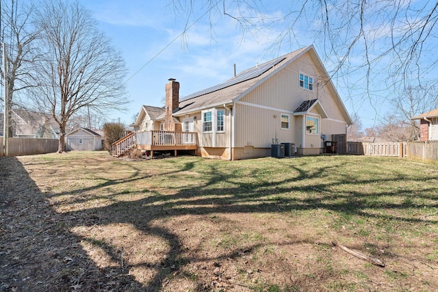 back of house featuring a lawn, a fenced backyard, a wooden deck, solar panels, and a chimney