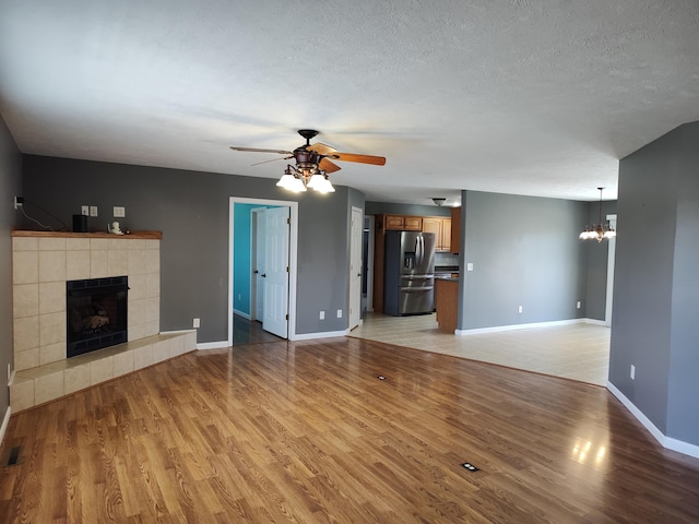 unfurnished living room featuring ceiling fan with notable chandelier, light wood-style flooring, a fireplace, and a textured ceiling