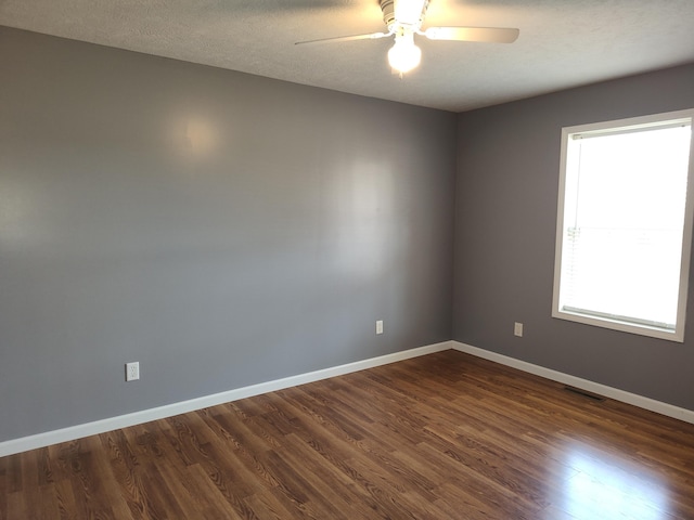 spare room with a textured ceiling, baseboards, dark wood-style flooring, and ceiling fan