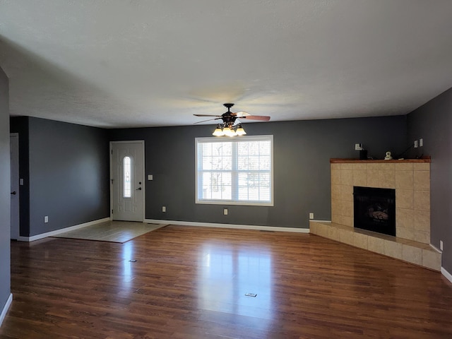 unfurnished living room with wood finished floors, a fireplace, baseboards, and ceiling fan