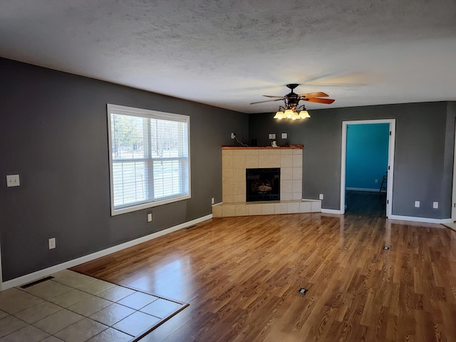 unfurnished living room featuring a textured ceiling, wood finished floors, baseboards, and a tile fireplace