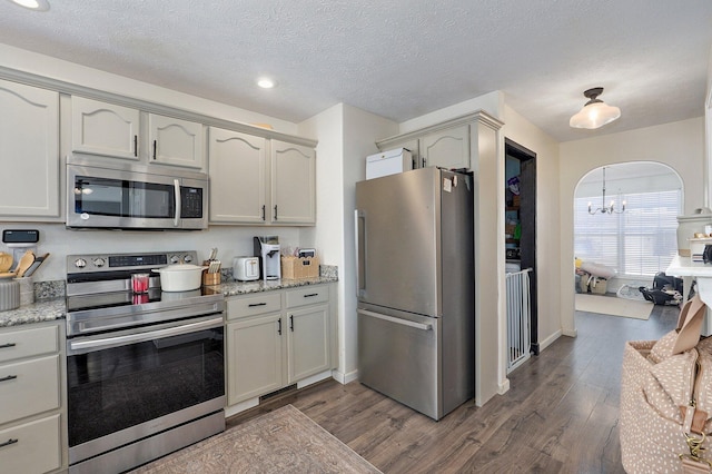 kitchen featuring stainless steel appliances, arched walkways, dark wood-style flooring, and light stone countertops