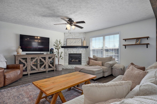 living area featuring a fireplace, a textured ceiling, a ceiling fan, and wood finished floors