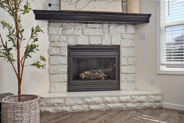 details featuring a stone fireplace, baseboards, visible vents, and wood finished floors