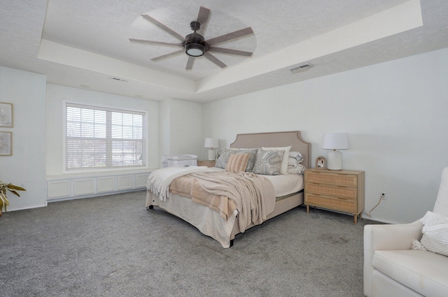 carpeted bedroom with visible vents, a textured ceiling, and a tray ceiling