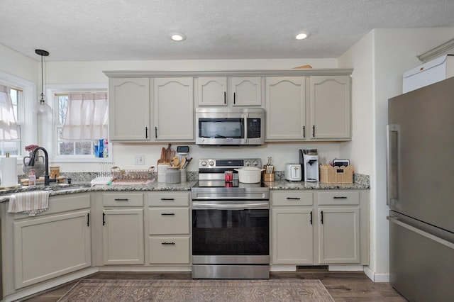 kitchen featuring light stone countertops, dark wood-style floors, appliances with stainless steel finishes, and a sink