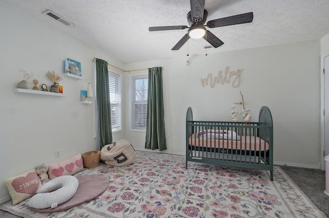 carpeted bedroom featuring visible vents, a crib, baseboards, ceiling fan, and a textured ceiling