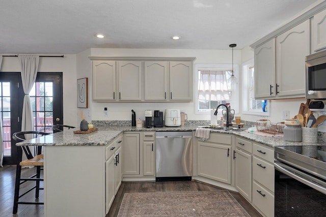 kitchen with a sink, a breakfast bar area, appliances with stainless steel finishes, a peninsula, and dark wood-style flooring