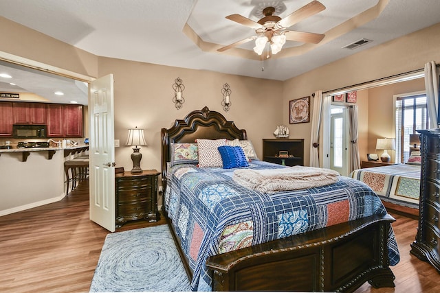 bedroom with visible vents, baseboards, a tray ceiling, and wood finished floors