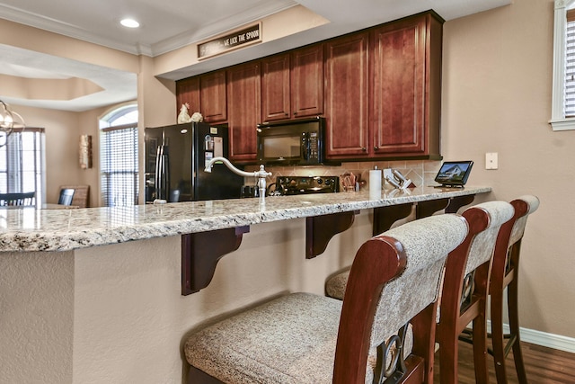 kitchen with a breakfast bar, black appliances, light stone counters, and backsplash