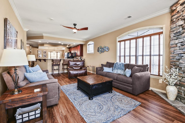 living area with visible vents, baseboards, ornamental molding, wood finished floors, and a ceiling fan