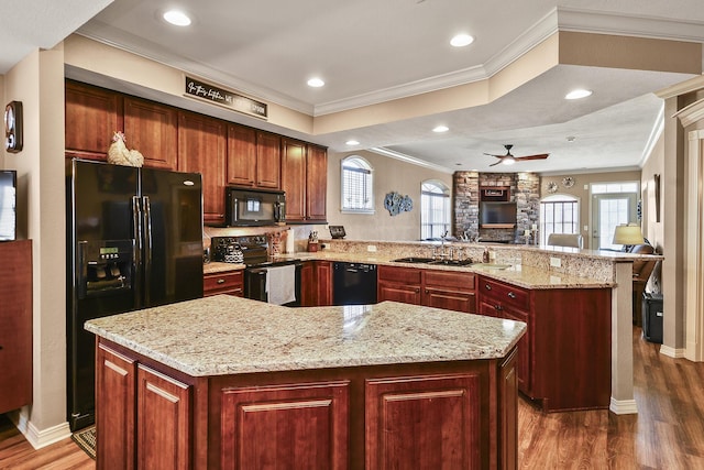 kitchen featuring black appliances, a sink, a kitchen island, wood finished floors, and a peninsula