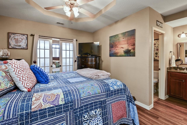 bedroom with visible vents, a ceiling fan, wood finished floors, baseboards, and a raised ceiling