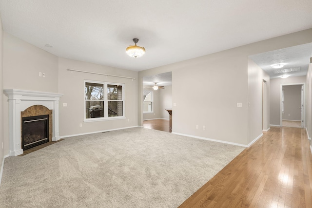 unfurnished living room featuring a premium fireplace, light carpet, light wood-style floors, and baseboards