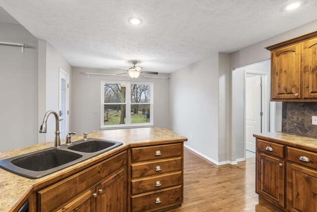 kitchen featuring light wood finished floors, backsplash, baseboards, light countertops, and a sink