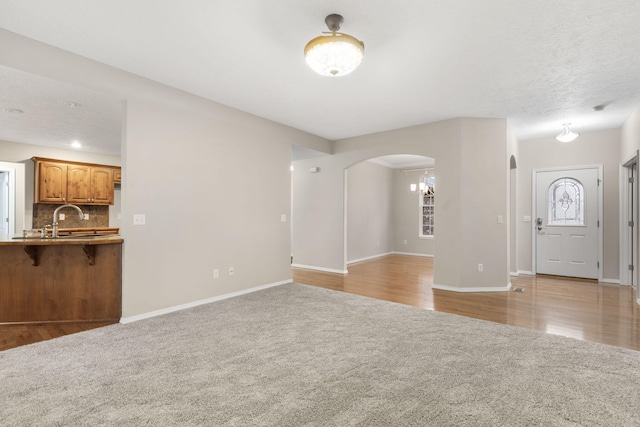 unfurnished living room with wood finished floors, baseboards, arched walkways, a sink, and carpet flooring