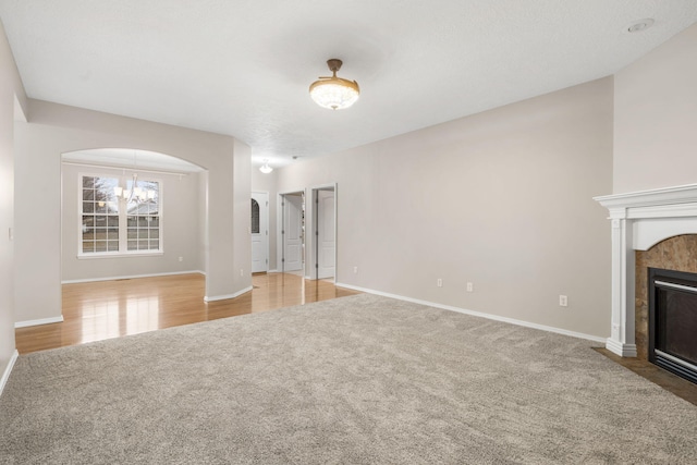 unfurnished living room featuring a tiled fireplace, arched walkways, baseboards, and carpet