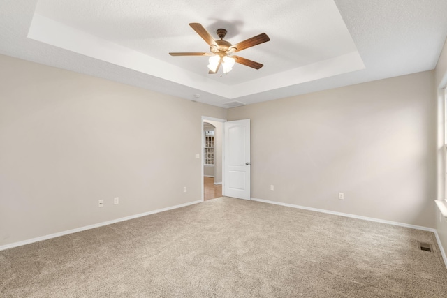 spare room featuring visible vents, baseboards, a tray ceiling, carpet floors, and a ceiling fan