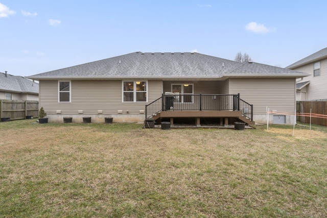 rear view of house with a shingled roof, a lawn, a deck, and fence