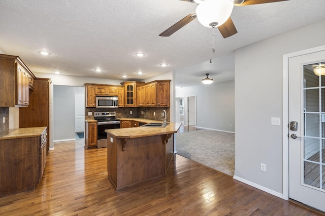 kitchen featuring backsplash, glass insert cabinets, a peninsula, stainless steel appliances, and a sink