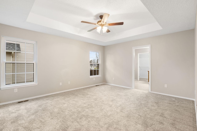 carpeted spare room with a ceiling fan, baseboards, visible vents, a tray ceiling, and a textured ceiling