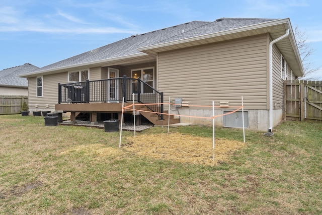 back of property with a deck, a yard, fence, and roof with shingles