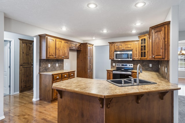 kitchen featuring glass insert cabinets, light countertops, appliances with stainless steel finishes, a peninsula, and a sink